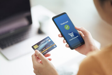 Young woman holding credit card and using smart phone for online shopping, internet banking, e-commerce, spending money, working from home concept