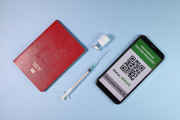 Digital international vaccine passport smart phone screen qr code app coronavirus covid 19 immunization red passport book small bottle disposable medical syringe needle on light sky blue background