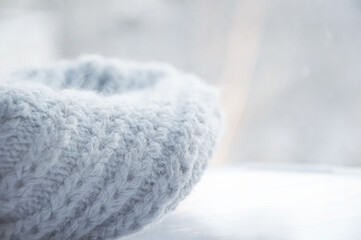 A gray knitted woolen scarf, neatly folded, against a light blurred background. Cozy winter background, warm in light colors. There is room for text.
