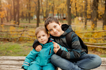 Obraz na płótnie Canvas Little brother with brother sit at the outdoor. Fraternal relations. Two happy boys in the woods. Cute brothers who are smiling happily together. Two brothers play outdoors in autumn, best friends.