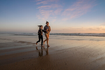 pretty young woman and little girl running on the beach at sunset