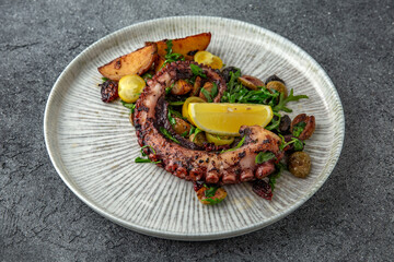 Grilled octopus with baked potatoes and vegetables. Ready menu for the restaurant. Neutral gray blue textured background