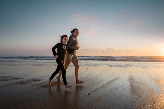 pretty young woman and little girl running on the beach at sunset