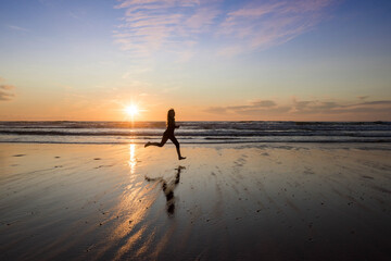 Fototapeta premium young girl running and jumping with happiness on the beach at sunset