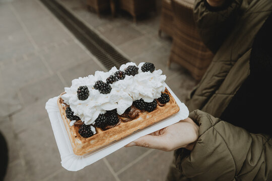 Detail of the Traditional Polish specialty gofry with whipped cream and blackberries on woman hand
