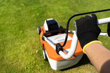 A woman gardener is trimming grass with the grass cutter and hands in gloves