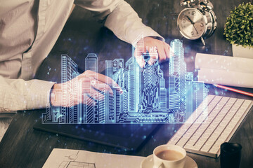 Double exposure of man's hands holding and using a digital device and city drawing.