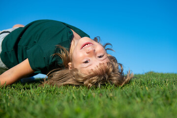 Sweet, happy child boy playing upside down on a grass in a park at a spring. Laughing, enjoying fresh. Funny kids.
