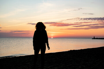 Fototapeta premium Female silhouette on the beach against the background of the sea surf and the rising sun. Resort concept.