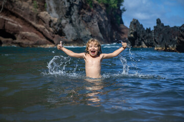 Child playing in ocean water. Kid jumping in the sea waves. Kids vacation on beach. Little excited boy swimming during summer holiday.
