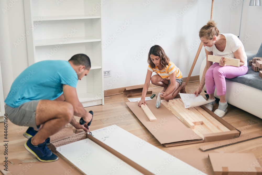 Wall mural mother, father, and daughter assembling furniture in new apartment, moving in and being hardworking.