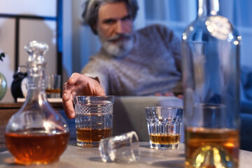 Senior man with glass of drink late in evening at home, closeup