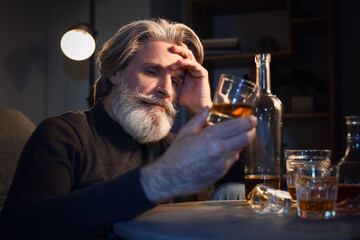 Drunk senior man with glass of whiskey late in evening at home