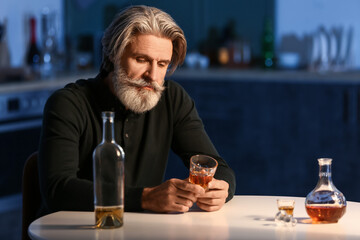 Drunk senior man with glass of drink in kitchen at night