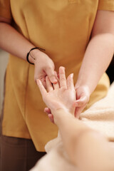 Close-up image of female therapist pressing specific spots on palm of young woman