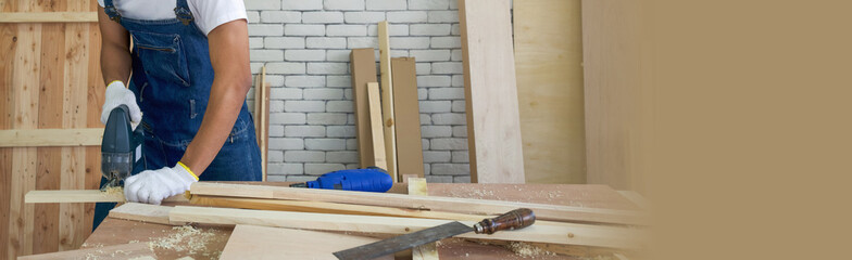 Carpentry use electric hand saw to cut plywood at the woodworking facility. A desk full of hand...