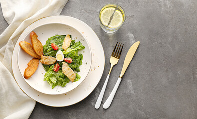Plate with Caesar salad and glass of water on grunge background