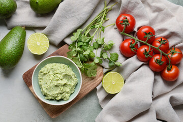 Bowl with tasty guacamole, tomato, avocado and lime on light background