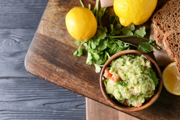 Bowl with tasty guacamole, lemon and parsley on wooden background