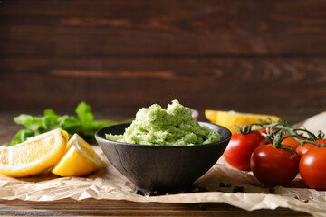 Bowl with tasty guacamole, lemon and tomato on wooden background, closeup
