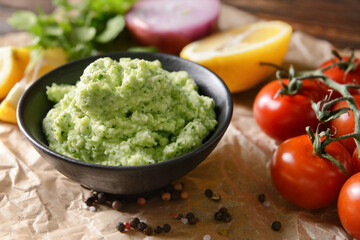 Bowl with tasty guacamole, lemon and tomato on parchment, closeup