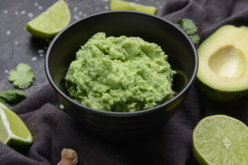 Bowl with tasty guacamole and lime on dark background