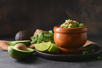 Bowl with tasty guacamole, avocado and lime on dark background