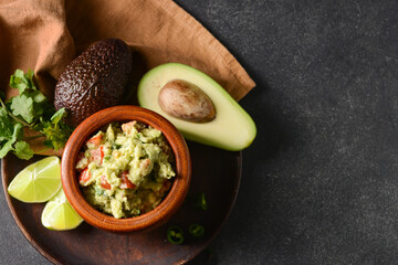 Bowl with tasty guacamole, avocado and lime on dark background