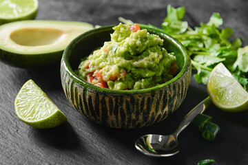 Bowl with tasty guacamole, avocado and lime on dark background, closeup