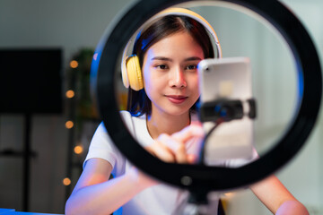 Smiling Young Asian woman wearing headset and live broadcasting on internet and reading comments...