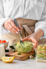 Woman cooking tasty guacamole on table, closeup