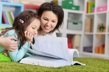 mother with daughter reading book while lying on floor