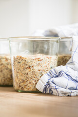 Brotteig von Vollkorn Brot mit Kürbiskernen, Haferflocken, Sonnenblumenkernen, Chia und Leinsaat roh im Glas für Einkochen, Vorrat und Speisekammer auf Tuch und Holz Hintergrund hell