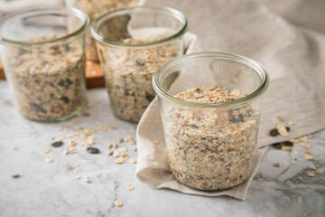 Brotteig von Vollkorn Brot mit Kürbiskernen, Haferflocken, Sonnenblumenkernen, Chia und Leinsaat roh im Glas für Einkochen und Vorrat auf Leinentuch, Holzbrett und Marmor Hintergrund hell