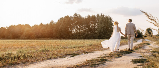 Bride and groom on wedding day hug and walking along the road to the forest at sunset