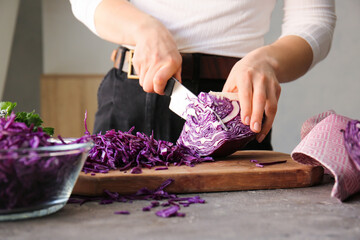 Woman cutting fresh purple cabbage on table