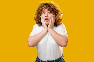 Omg face. Shocked woman. Obesity struggle. Body positive. Surprised excited overweight girl with curly hair hands grasping head isolated in yellow background. - obrazy, fototapety, plakaty