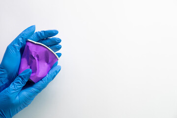 Pollution reduction. Planet protecting. Waste recycling. Hands in medical gloves holding purple plastic litter cup isolated on white copy space background.