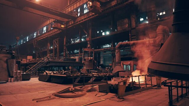 Blast furnace in foundry with smoke and light from molten metal in factory interior, heavy industry.