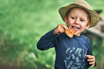 Boy in straw hat eats grilled chicken wing in green yard