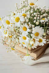 Bouquet of beautiful chamomile flowers and books on light background, closeup