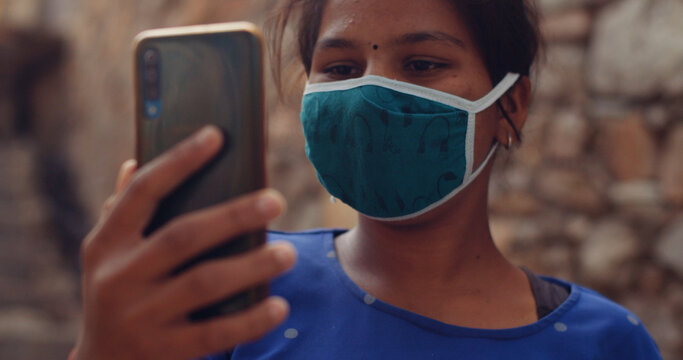 Shallow focus of an Indian girl wearing a face mask and taking a picture on her smartphone