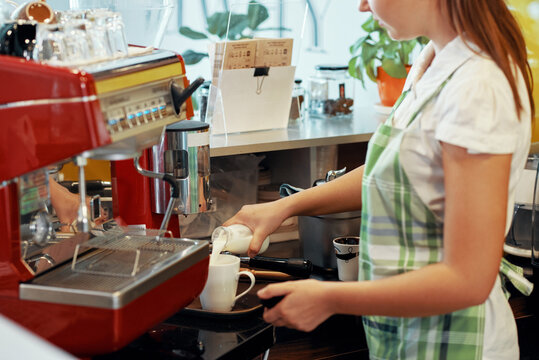 Close-up image of female barista pouring fresh milk or cream in cup of coffee for customer
