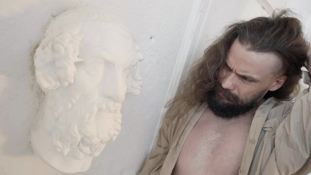 creative crisis of male charismatic artist, man is learning on white wall in workshop