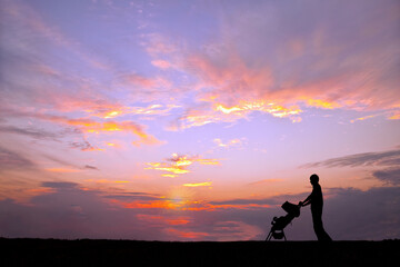 夕日の空を背景にベビーカーを押し散歩をする若い男性