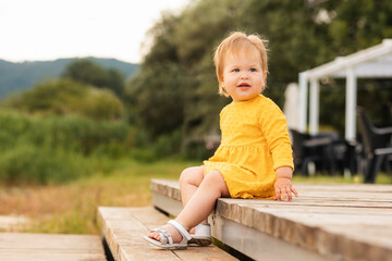 Summertime. Pretty smiling little girl in yellow dress sitting on the steps. Outdoors. The concept...