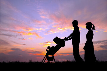 夕日の空を背景にベビーカーを押し散歩をする若い夫婦