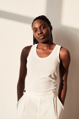 Vertical portrait of young African-American woman looking at camera while posing against white in...