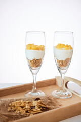 Tray with two glasses with delicious breakfast made of granola, fresh yogurt and mango pieces
