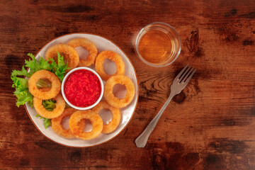 Calamari rings with wine and copy space. Deep fried squid rings with green salad leaves and a red sauce, shot from above on a dark rustic wooden background